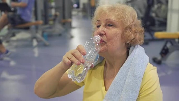 疲倦的老年妇女在训练后喝水