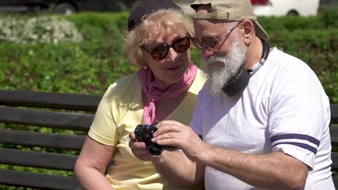 时尚的成熟夫妇坐在公园的长凳上看着相机上的照片