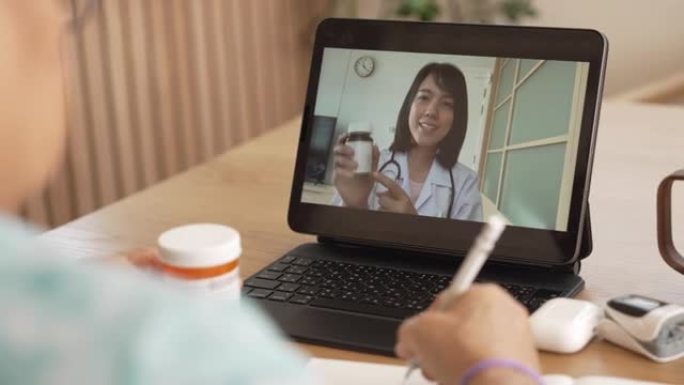 资深亚洲女性在与医生在线咨询时做笔记。