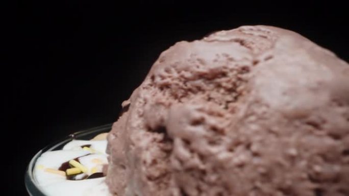 一个装有巧克力冰激凌球和糖粉的玻璃杯在黑色背景上旋转，特写镜头。全景