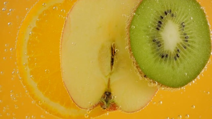 在透明水中的橙色，苹果和猕猴桃切片，在橙色背景上的气泡中。