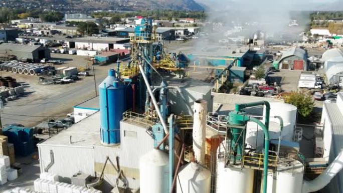 空中近距离拍摄工业综合体上的大型蓝色筒仓和烟囱向大气中吹出烟雾