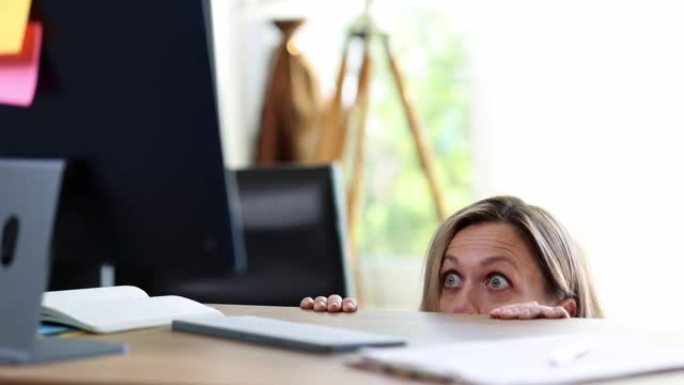 惊讶的兴奋受惊的女人从桌子后面偷看，看着电脑屏幕的肖像
