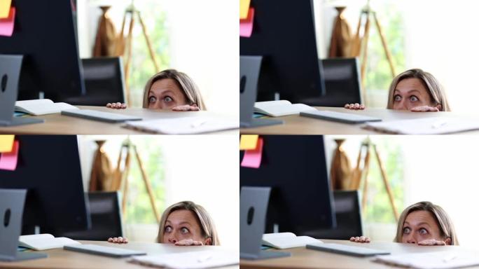 惊讶的兴奋受惊的女人从桌子后面偷看，看着电脑屏幕的肖像