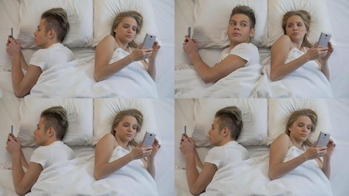 年轻夫妇背靠背躺在床上在手机上上网，冷漠