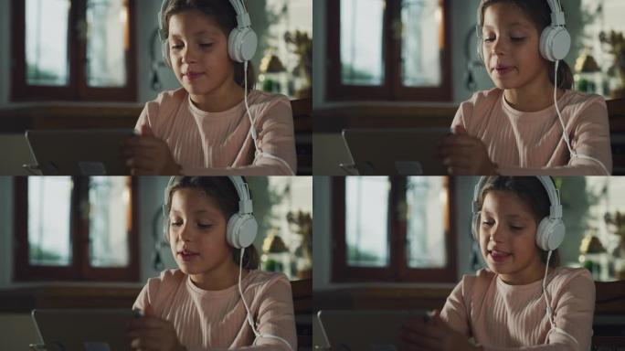 小女孩在数字平板电脑上录制视频，通过耳机收听的真实镜头。厨房里的女学生在享受周末的早晨，使用技术，进