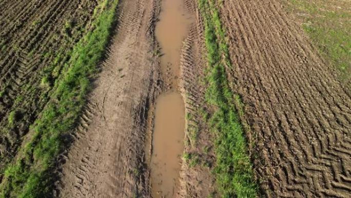 空中无人驾驶飞机在乡村的土路上飞过水，穿过泥泞的水坑