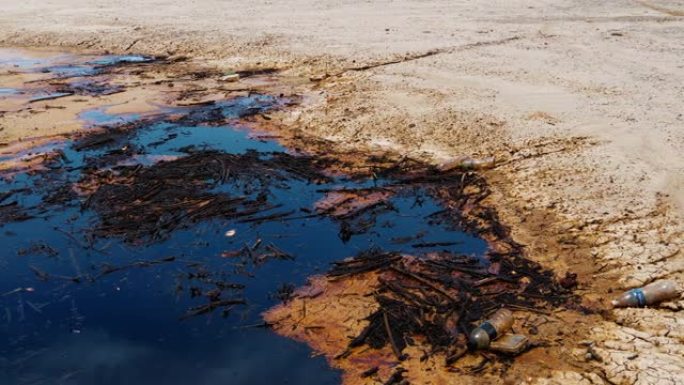 石油污染旁边的石油井泵杰克在秘鲁沙漠抽油旁边的一个小湖的水，背景是多云的蓝天和沙漠丘陵