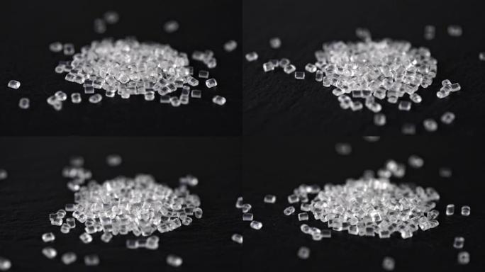 透明的塑料颗粒在黑色背景上倾泻而下。聚合物颗粒。