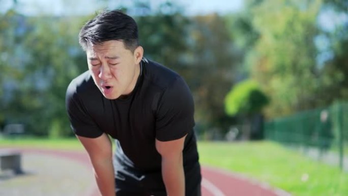 一名成年亚洲跑步者在城市体育场的跑步机上快速冲刺后呼吸急促。穿着运动服的运动员倾斜