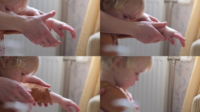 母亲的手在一个快乐的婴儿身上涂抹奶油。妈妈按摩一个微笑的蹒跚学步的孩子