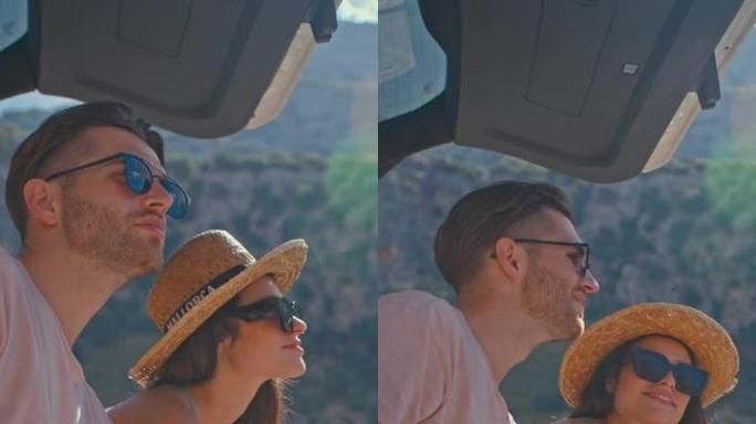 一对相爱的夫妇坐在湖边的一个大汽车后备箱里一起露营。喝茶垂直视频