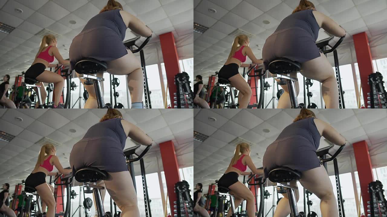 疲惫的超重女性在运动俱乐部慢慢骑健身车