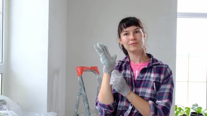 女人戴上建筑手套，保护他的手免受梯子旁边的油漆。用自己的双手进行房屋的建筑工程和美容维修，墙面粉刷，