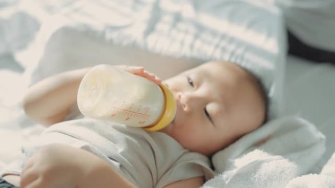 可爱的男婴在床上喝奶瓶里的牛奶。