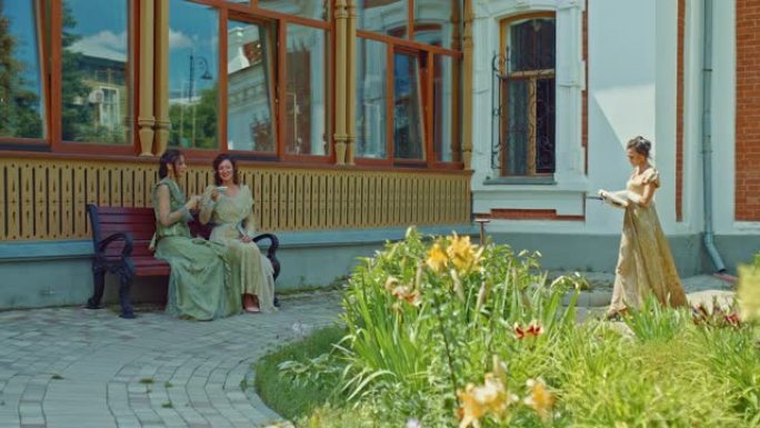 社会女士散步、喝茶和看书。穿着优雅的蕾丝连衣裙的女士们在一座古老的豪宅的院子里聊天，这是贵族的休闲。