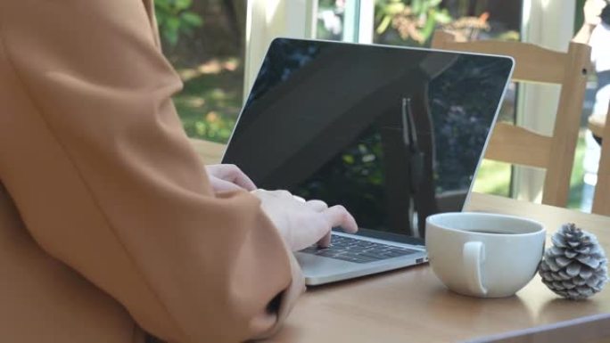 关闭女商人手打字笔记本电脑在绿色花园咖啡馆喝黑咖啡杯。女人的手喜欢在家工作喝热咖啡。有黑咖啡或热巧克