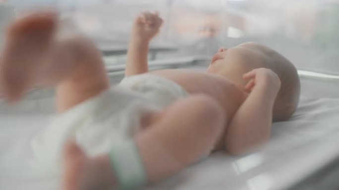 可爱的高加索新生婴儿躺在产科医院的摇篮里。一个小小的顽皮和精力充沛的孩子的肖像，腿上有名字ID标签。