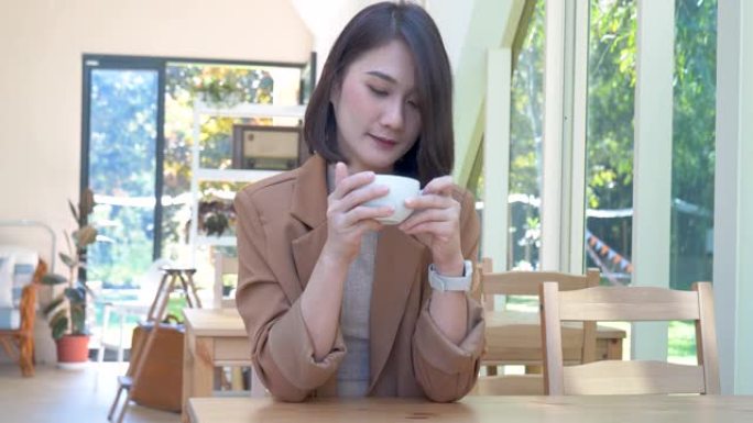 亚洲妇女在绿园咖啡馆喝黑咖啡手捧杯。年轻女子笑脸爱喝咖啡。美丽的女人在咖啡店里喝红茶，拿着新鲜的杯子