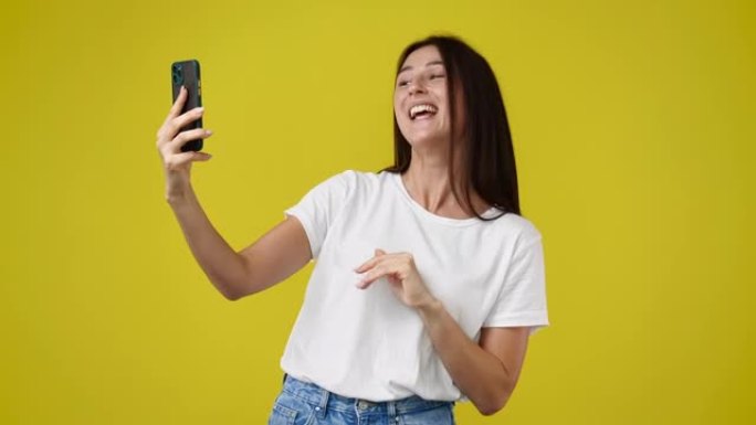4k视频，可爱的女孩使用手机，在黄色背景上挥手打招呼。