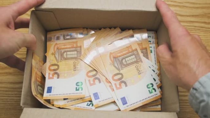 男性双手打开装满欧元现金的纸箱。俯视图，特写。隐性金钱、遗产、礼物、影子经济的概念。