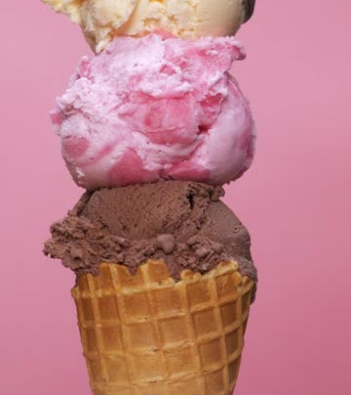 垂直视频前视图，在草莓顶部和粉红色背景上的巧克力冰淇淋蛋卷上舀香草冰淇淋。