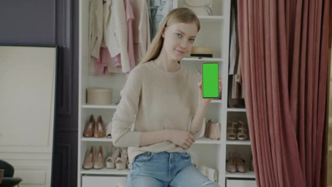 手持智能手机的年轻女子慢动作肖像，色键绿色屏幕站在现代时尚精品店