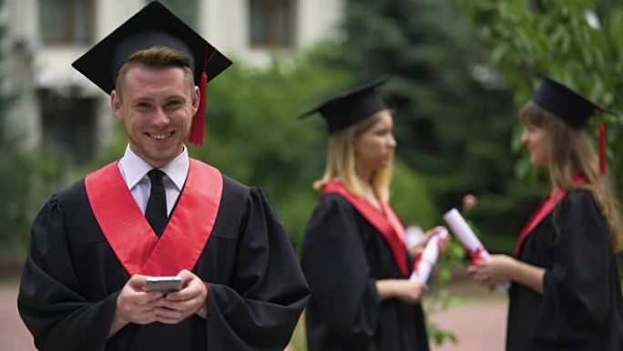男毕业生在手机上打字留言，微笑对着镜头，毕业