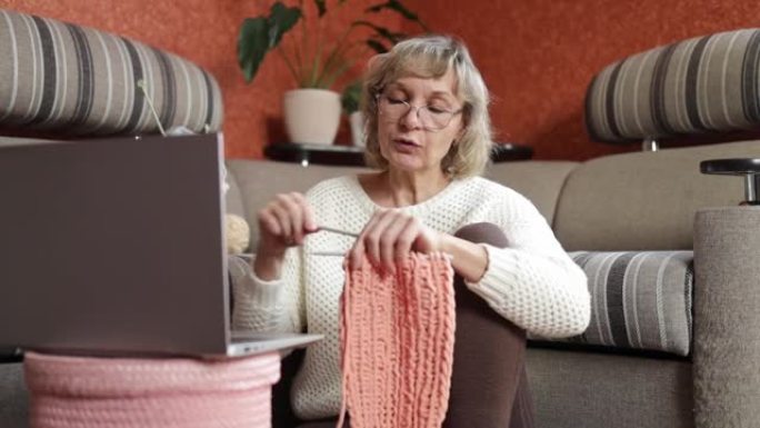 女人通过笔记本电脑上的视频链接与朋友或亲戚交流，编织在织针上。