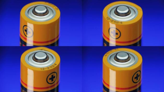 碱性电池在蓝色背景上旋转。加号是特写