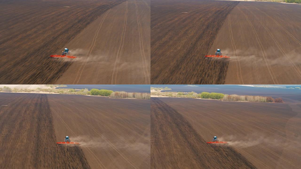 一辆蓝色的拖拉机，带有宽红色的耙和白色的旗帜，在地面上播种农作物。厚厚的灰尘从耙和拖拉机中冒出来。顶