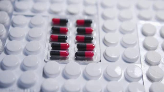 红色和黑色药丸躺在白色水泡之间，片剂在桌上，癌症药物的临床试验，具有活性物质和安慰剂作用的药物