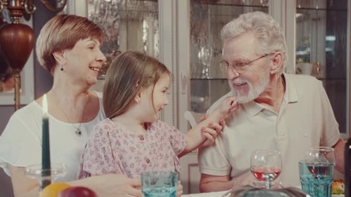 在一次家庭晚宴上，一个小孙女和她的祖父玩耍，拉着胡须。一个女孩和一个老人在家庭餐桌上开玩笑。好心情。
