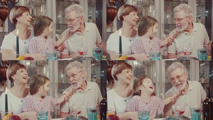 在一次家庭晚宴上，一个小孙女和她的祖父玩耍，拉着胡须。一个女孩和一个老人在家庭餐桌上开玩笑。好心情。