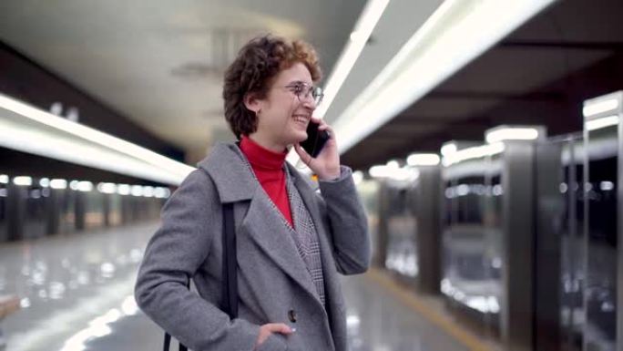 快乐的年轻女子站在地铁站台上在智能手机上聊天。