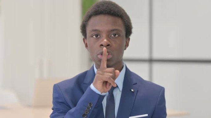 年轻的非洲商人用手指指着嘴唇，要求保持沉默