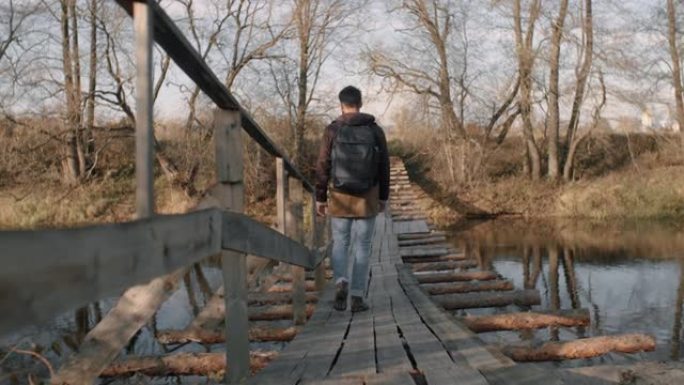 男子在傍晚的阳光下沿着河上的木吊桥行走，享受秋天的风景