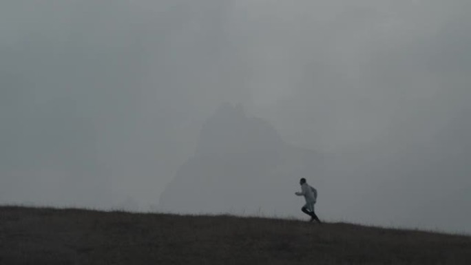 一个人沿着山顶奔跑，背景是在干燥的秋草上布满薄雾的山脉。与自然融为一体的乐趣。健康的生活方式。在大自