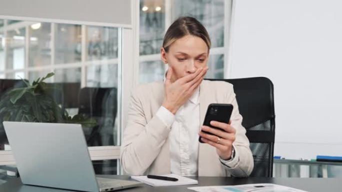 悲伤疲惫的女人坐在办公桌前拿着智能手机感到不快乐负面情绪不安通过收到短信女人的可怕消息看着屏幕感到糟