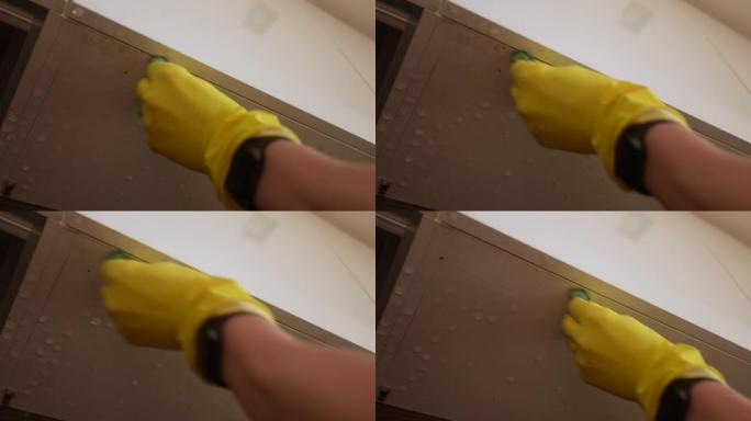 戴着手套的无法识别的男性的特写低角度视图使用蒸汽清洁器用热蒸汽处理肮脏的厨房搁板底部，用软海绵擦拭