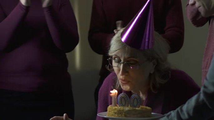 老妇人在100生日聚会上吹灭蛋糕蜡烛，志愿者支持