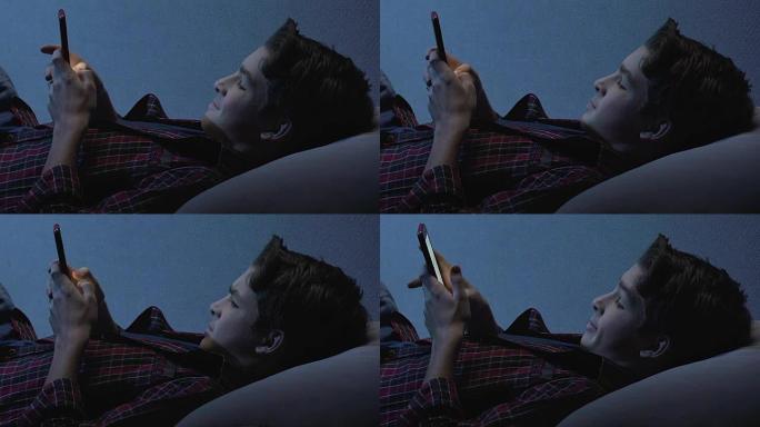 不听话的男孩在夜间在智能手机上上网，小工具成瘾
