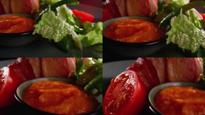 将热而油腻的火腿切片放在带有萨拉特，番茄和酱汁碗的盘子上-特写