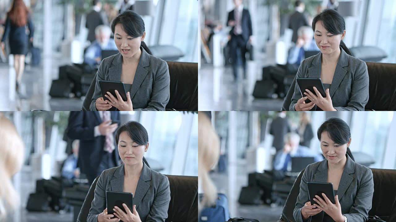 DS亚洲妇女坐在机场的商务休息室时，通过平板电脑进行视频通话