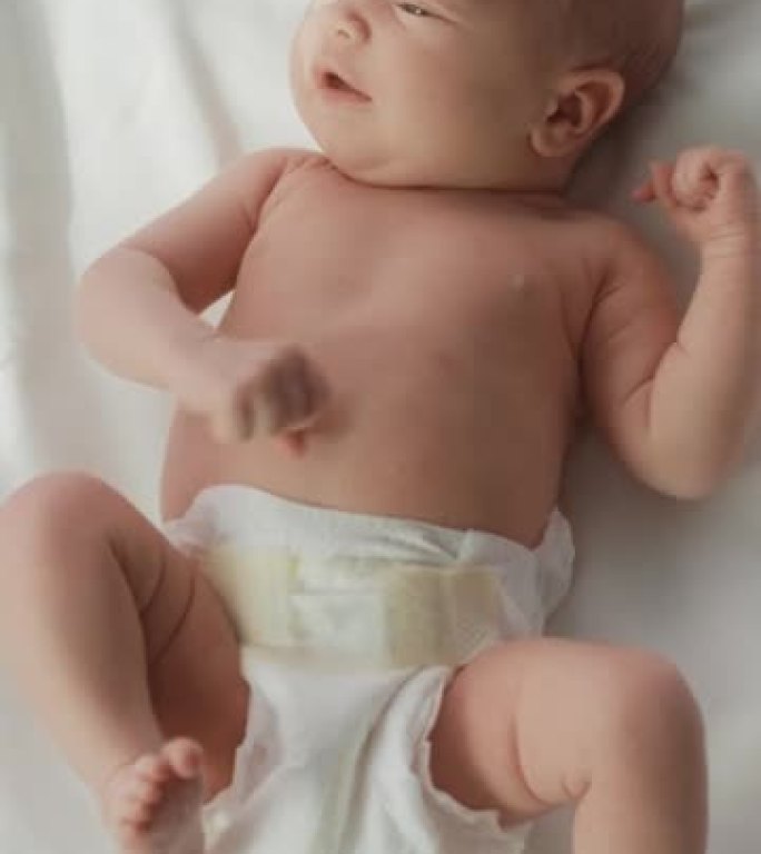 垂直屏幕: 可爱的高加索新生儿躺在托儿所的病床上。顽皮健康的小宝宝。医疗保健、生育和生育概念。自上而