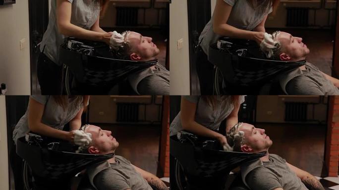一个女人在理发店洗头，留着胡须的男人用洗发水和护发素。洗掉洗发水水