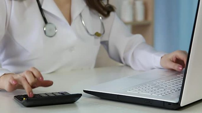 女医生在笔记本电脑上填写健康保险表格，计算