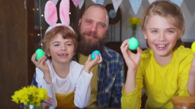 复活节家庭传统。父亲和两个白种人快乐的孩子，他们的兔子耳朵在家里坐在一起，玩复活节装饰的鸡蛋。