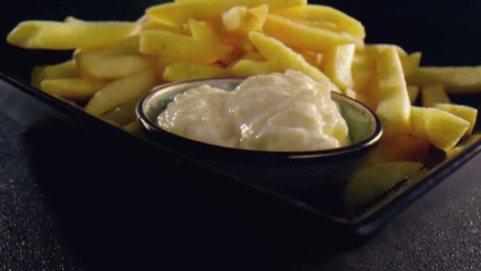 一堆美味的薯条放在带奶油大蒜酱蘸碗的背板上-特写