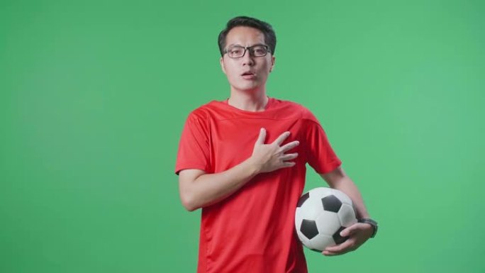 亚洲男子在绿屏背景上欢呼足球时唱着国歌